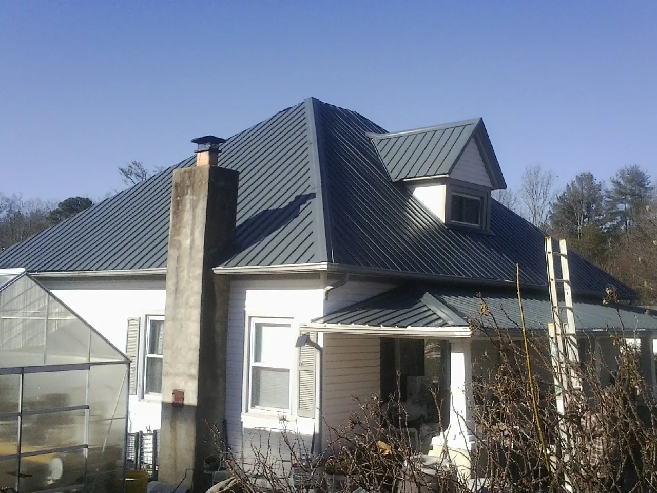 Dark blue standing seam metal roof on a white farmhouse with dormer — Slate & Tile Roof Repair by Roofing Brothers in Bates City