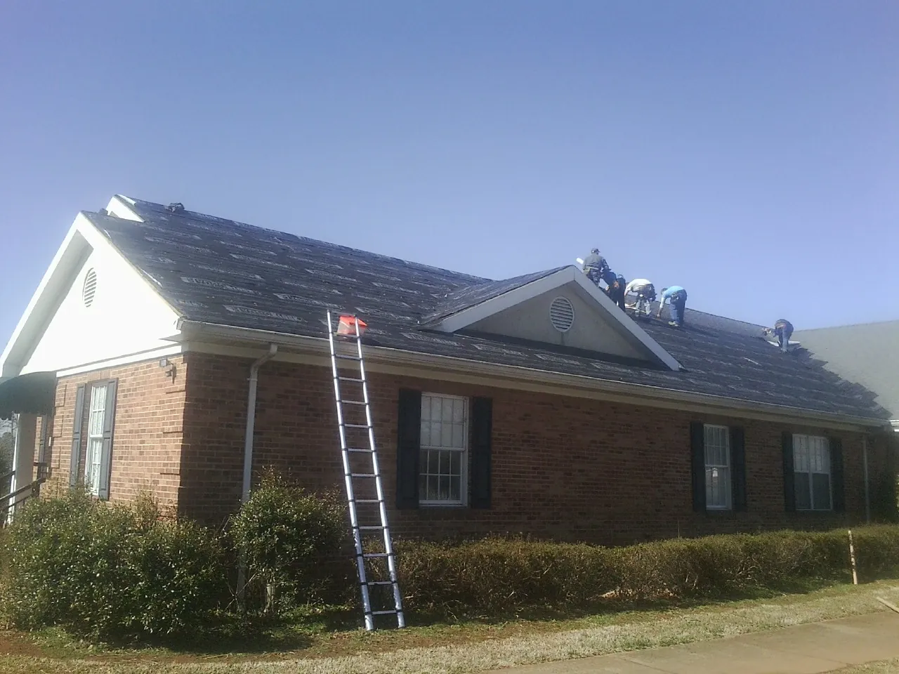 Crew tearing shingles off a brick ranch roof with a ladder set — Emergency Roof Repair work by our crew in Bates City
