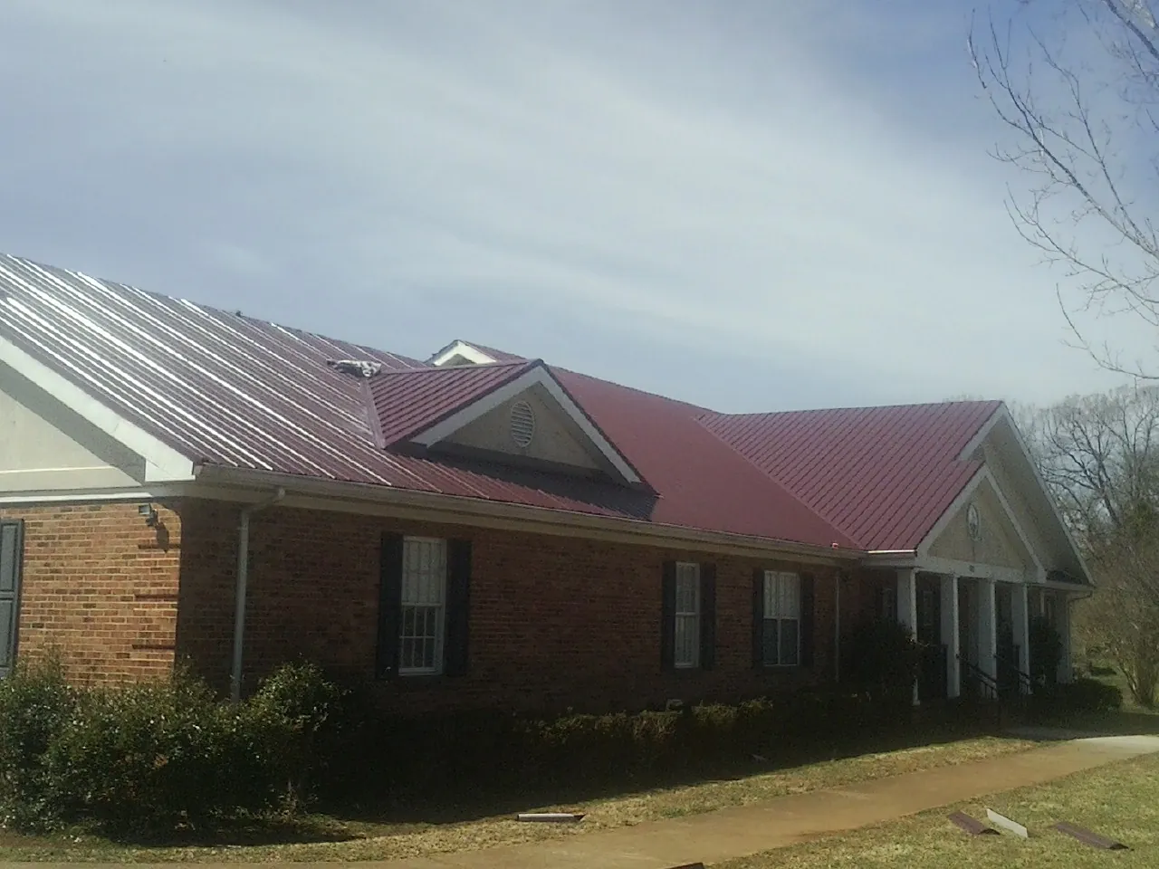 Red metal roof with gabled entries on a long brick building, from a Hail Damage Roof Repair job in Bates City
