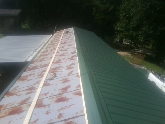 Old rusted panels beside newly installed green metal roofing — Wind Damage Roof Repair by Roofing Brothers in Bates City