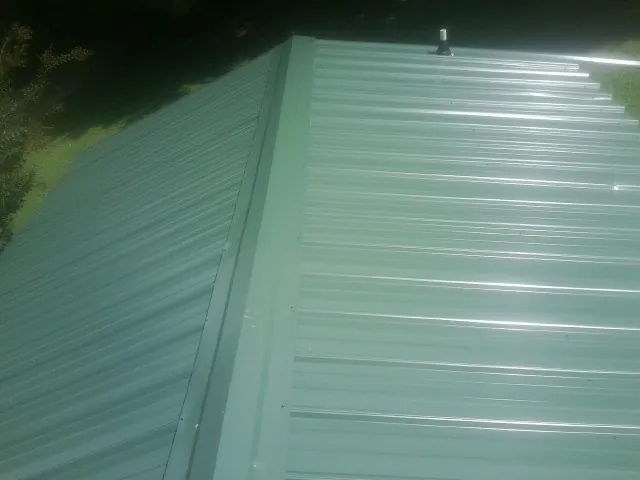 New green metal panels meeting at the ridge of a roof — Flat Roof Repair work by our crew in Bates City