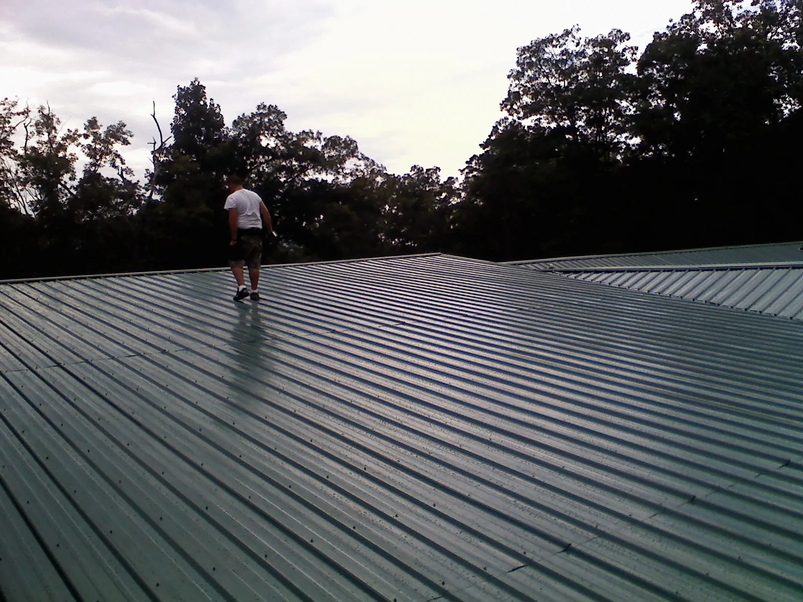 Roofer walking a wide expanse of new green metal roofing in Bates City