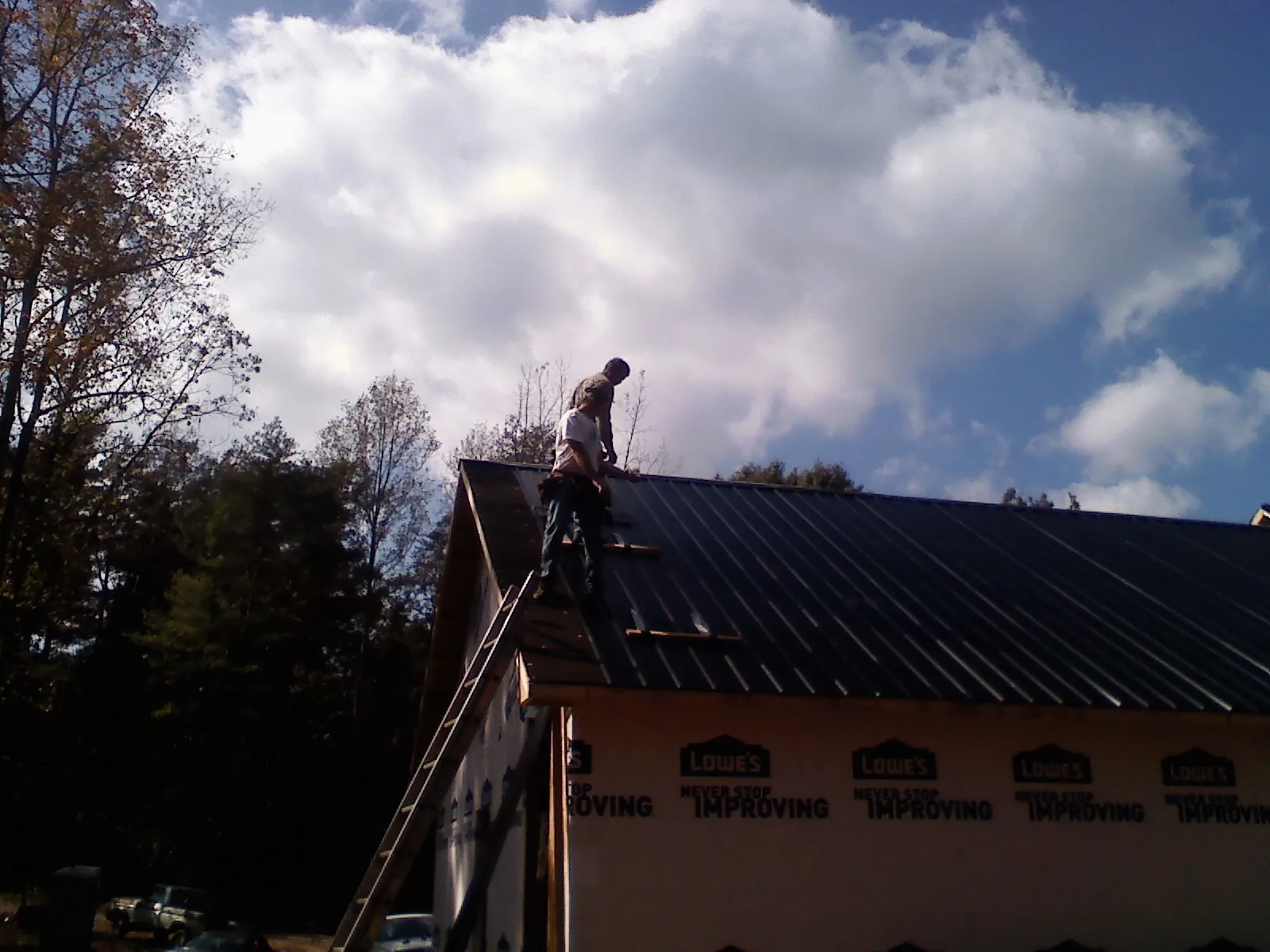 Roofer fastening dark metal panels high against a cloudy sky, from a Roof Inspection job in Bates City