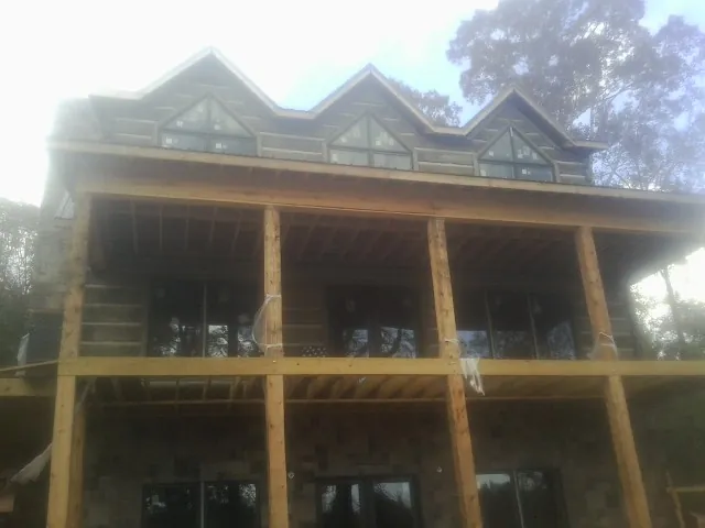 Dormers and porch framing on a large log home under construction — Roof Coating work by our crew in Bates City