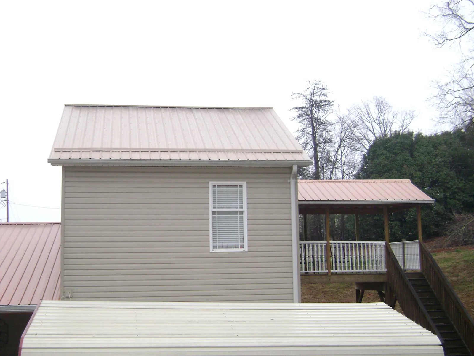 Tan metal roofs on a two story addition and attached porch, from a Roof Replacement job in Bates City